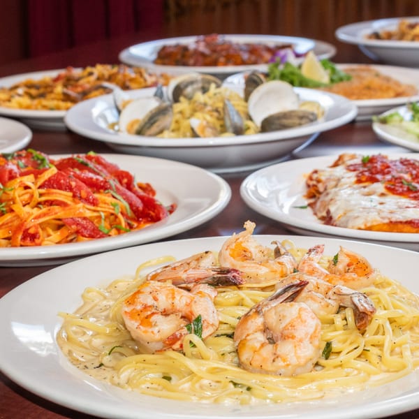 A table laden with various Italian dishes, including shrimp scampi, pasta with red sauce, and clams.