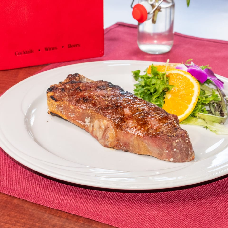 Grilled steak with a side salad, orange slices, and a purple orchid on a white plate.