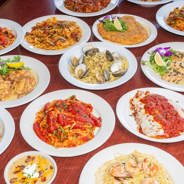 A table filled with various Italian dishes, including pasta with clams, chicken cutlets, and red sauce pasta.