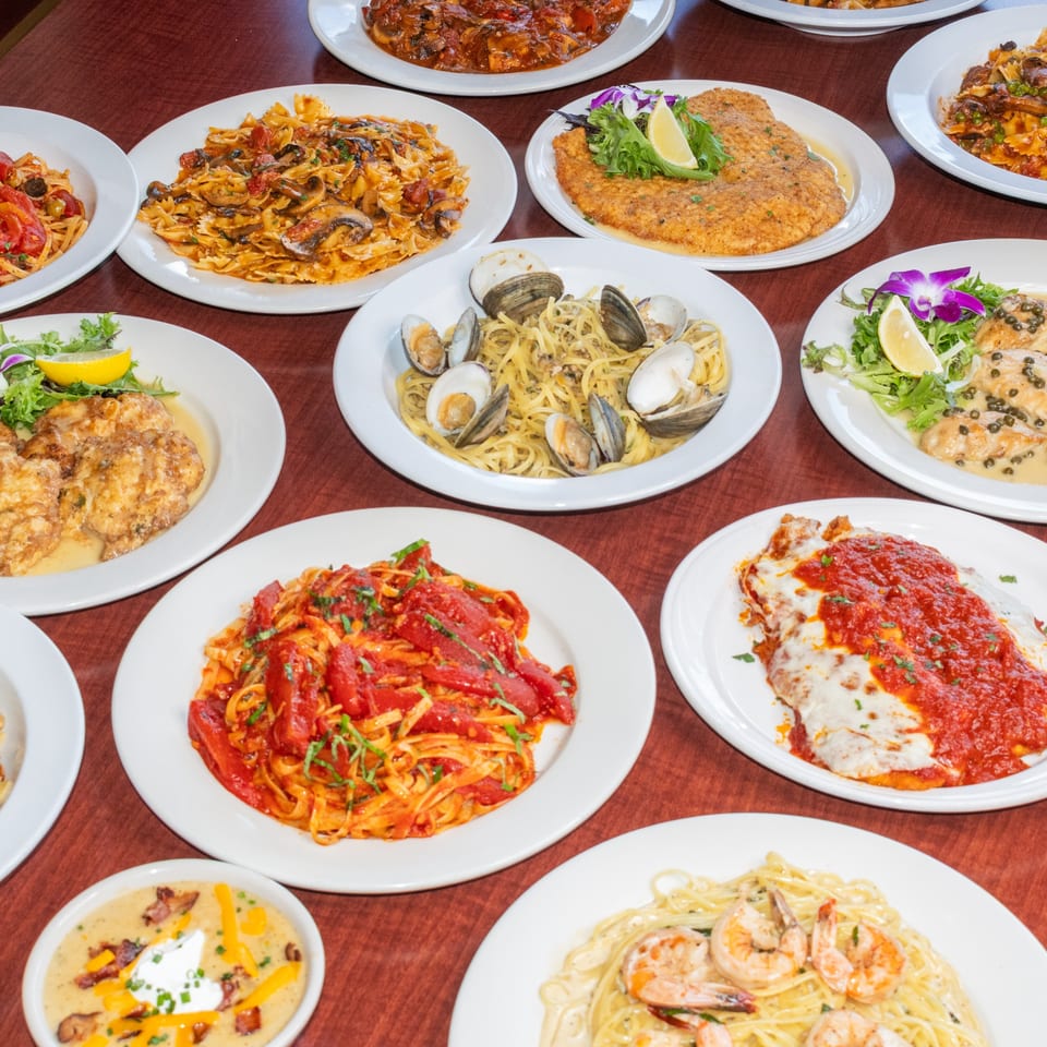 A table filled with various Italian dishes, including pasta with clams, chicken cutlets, and red sauce pasta.