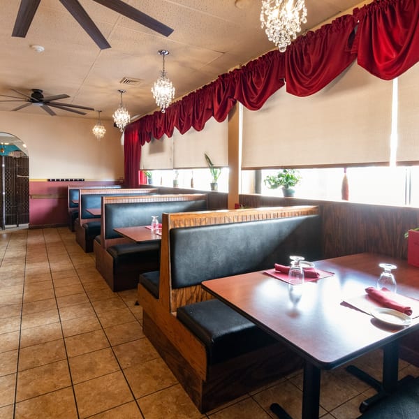 Empty Sorrento Restaurant dining room with black booths, wooden tables, red napkins, and chandeliers.