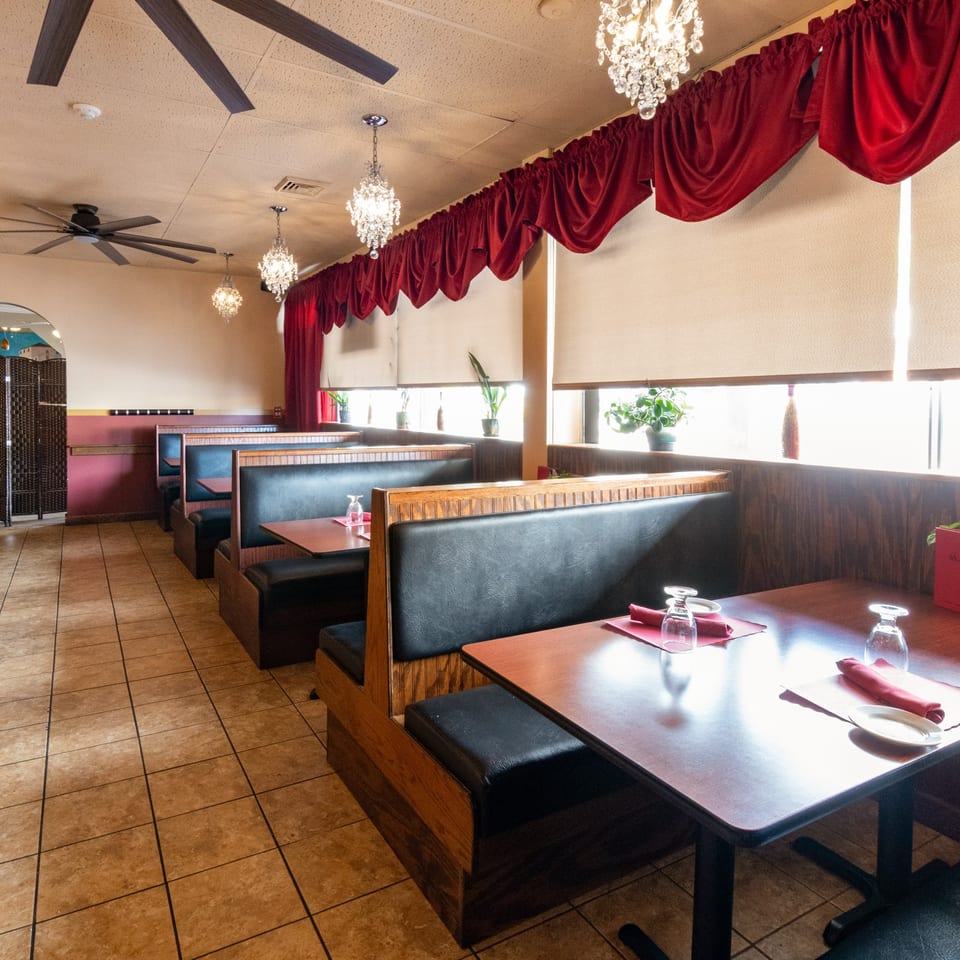 Empty Sorrento Restaurant dining room with black booths, wooden tables, red napkins, and chandeliers.