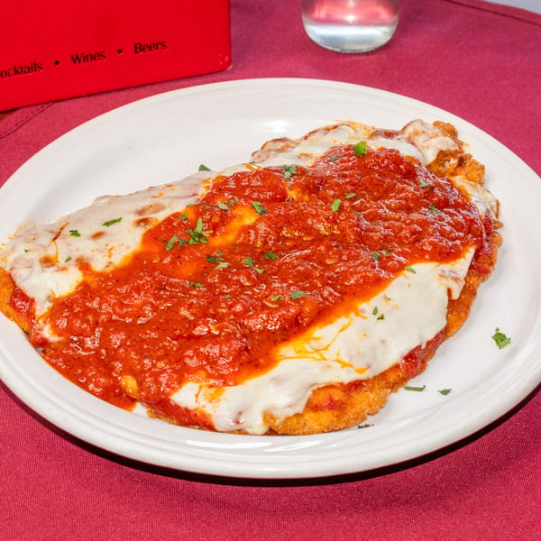 Chicken Parmesan with melted mozzarella cheese and red sauce, garnished with parsley on a white plate.