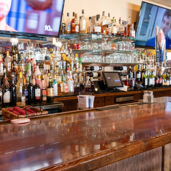 A well-stocked bar at Sorrento Restaurant with bottles of liquor, wine, and two TVs showing sports.