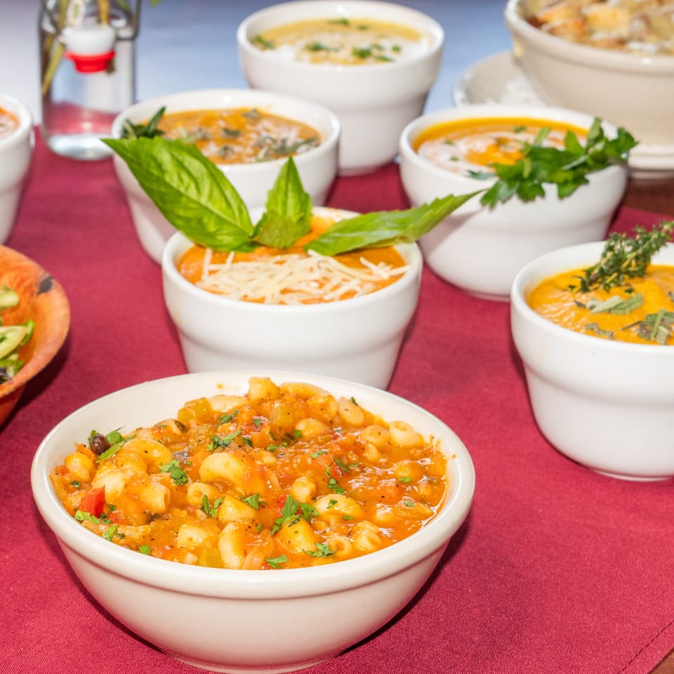 Multiple bowls of Italian soups and pasta, including minestrone, on a red tablecloth at Sorrento Restaurant.