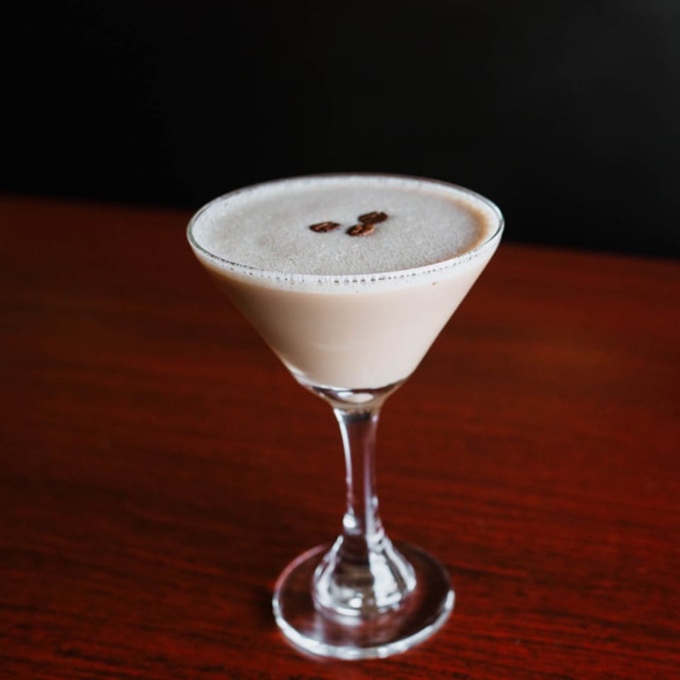 Espresso martini with coffee beans on top, served in a martini glass on a wooden table.
