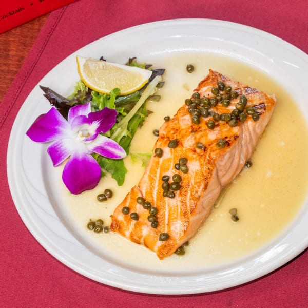 Pan-seared salmon with capers and lemon butter sauce, served with a side salad and orchid.