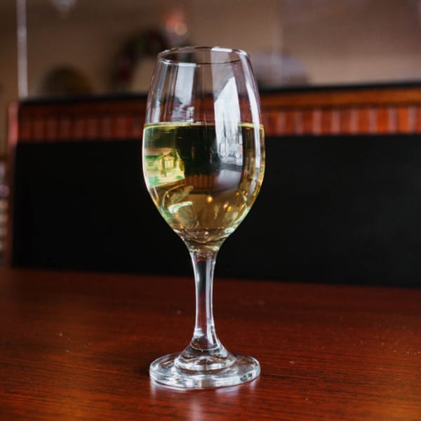 A glass of white wine sits on a dark wooden table at Sorrento Restaurant.