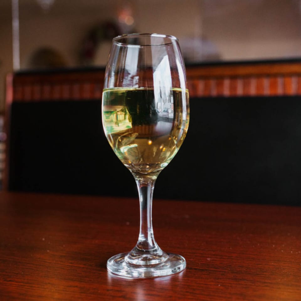 A glass of white wine sits on a dark wooden table at Sorrento Restaurant.